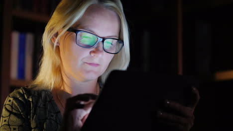 mujer en biblioteca con tableta en la noche