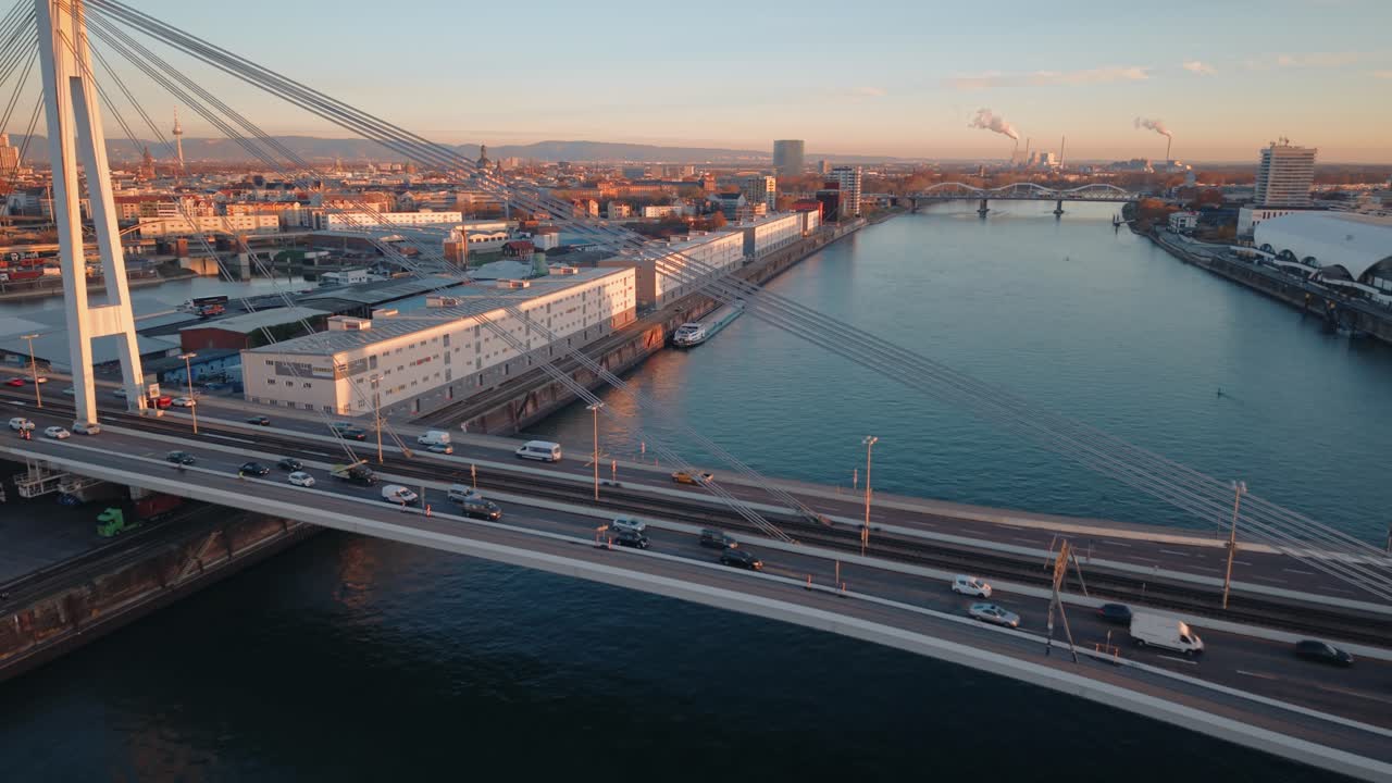 Mannheim Port Sunset Flyover: Golden Hour Aerial of Kurt-Schumacher-Bridge Traffic and Industrial Harbor Warehouses on the Rhine River, Germany