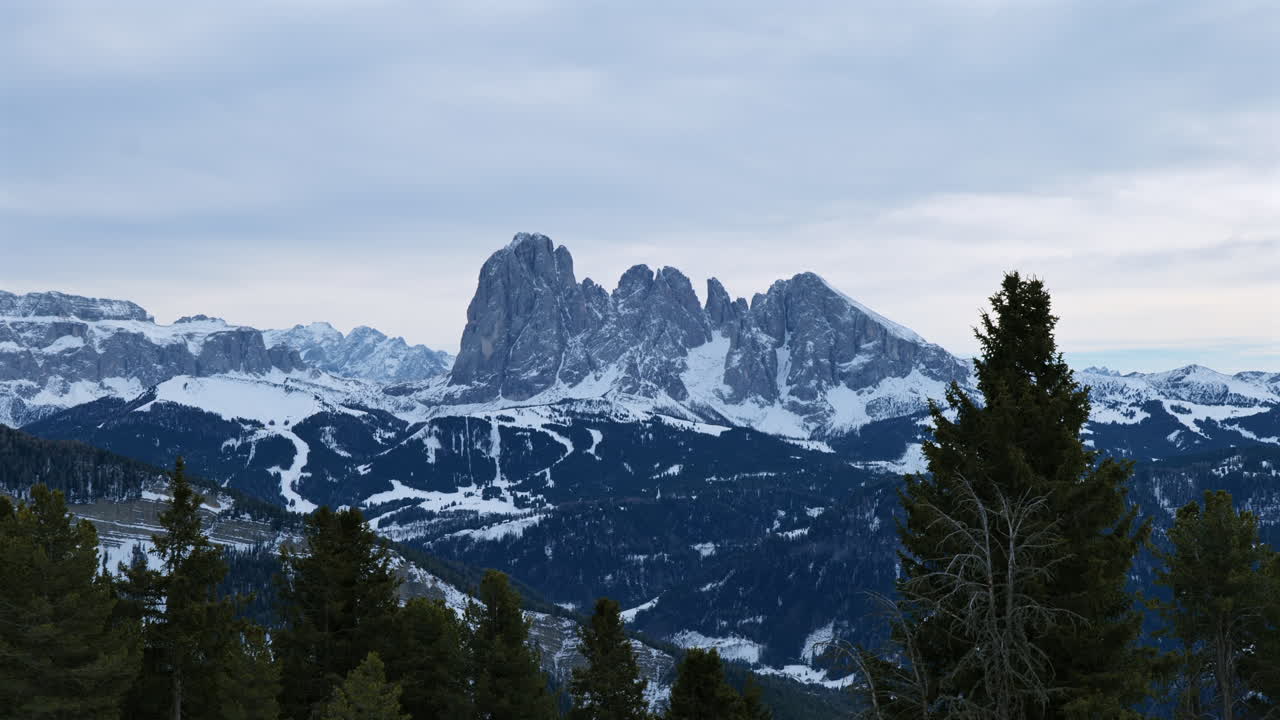 vista panorámica de las montañas dolomitas cubiertas de nieve y un exuberante bosque de pinos bajo un cielo nublado