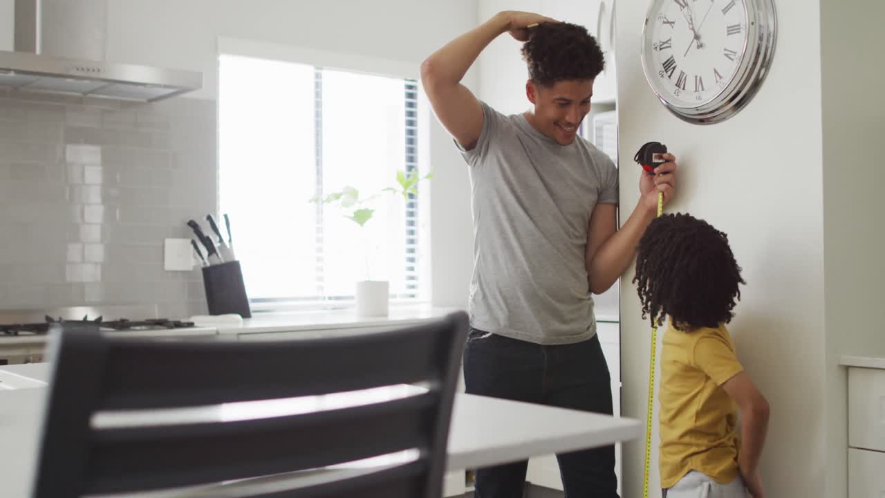 Happy biracial man and his son measure height in kitchen