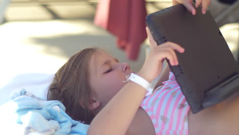 caucasian girl in bathing suit laying on lounger holding tablet screen