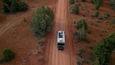 An-RV-drives-along-a-dirt-road-in-the-red-rock-southwest-of-Utah,-filmed-from-above-and-behind