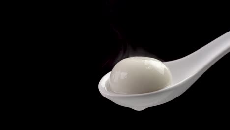 tangyuan rice dumpling ball with hot steam in a white spoon over black background.
