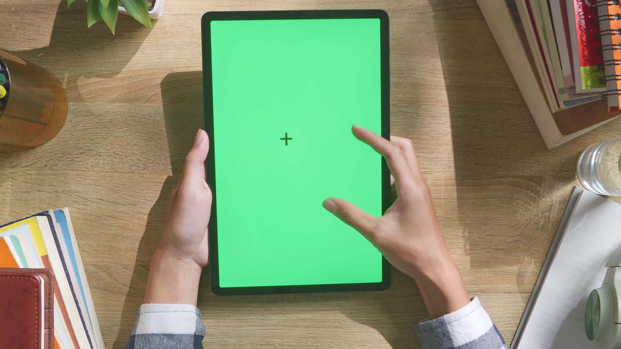 vista de arriba hacia abajo de una computadora portátil con pantalla verde simulada pantalla chromakey en un escritorio de oficina de madera al lado de la libreta con bolígrafos, gafas y un vaso de agua.