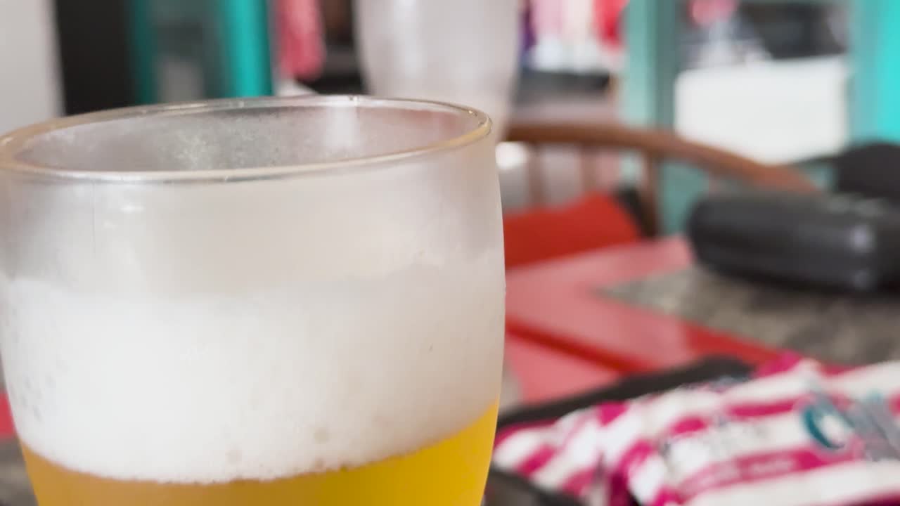 primer plano de un vaso de cerveza helado con burbujas en ascenso, colocado en una mesa con elementos de fondo coloridos