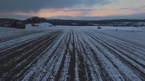 a rural field surrounded by trees in winter in bavaria, germany, with snow on the ground seen from above, aerial drone footage while sunset with red clouds and sky