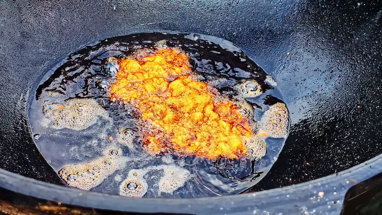 Deep-frying golden, battered fish in bubbling hot oil inside a dark cast-iron pan