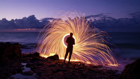 person light painting with steel wool by the ocean at twilight