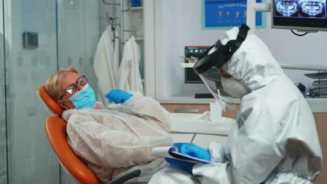 asistente de dentista en traje de vestir interrogando a una mujer mayor