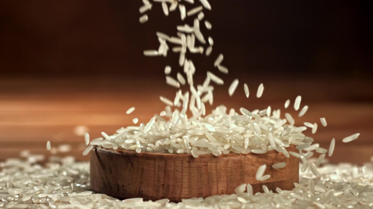 Witte rijstkorrels vallen in een houten kom in slow motion