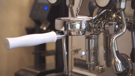 Barista-attach-portafilter-with-grinded-beans-on-shiny-coffee-machine