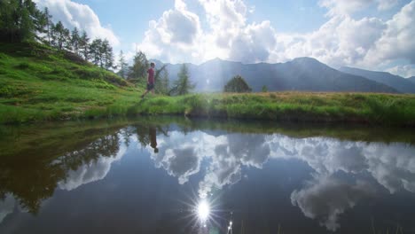 A-beautiful-sky-reflected-in-a-small-lake-in-the-Italian-alps-while-a-young-guy-walk-through-the-screen-in-slow-motion