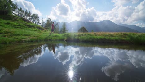 a beautiful sky reflected in a small lake in the italian alps while a young guy walk through the screen in slow motion