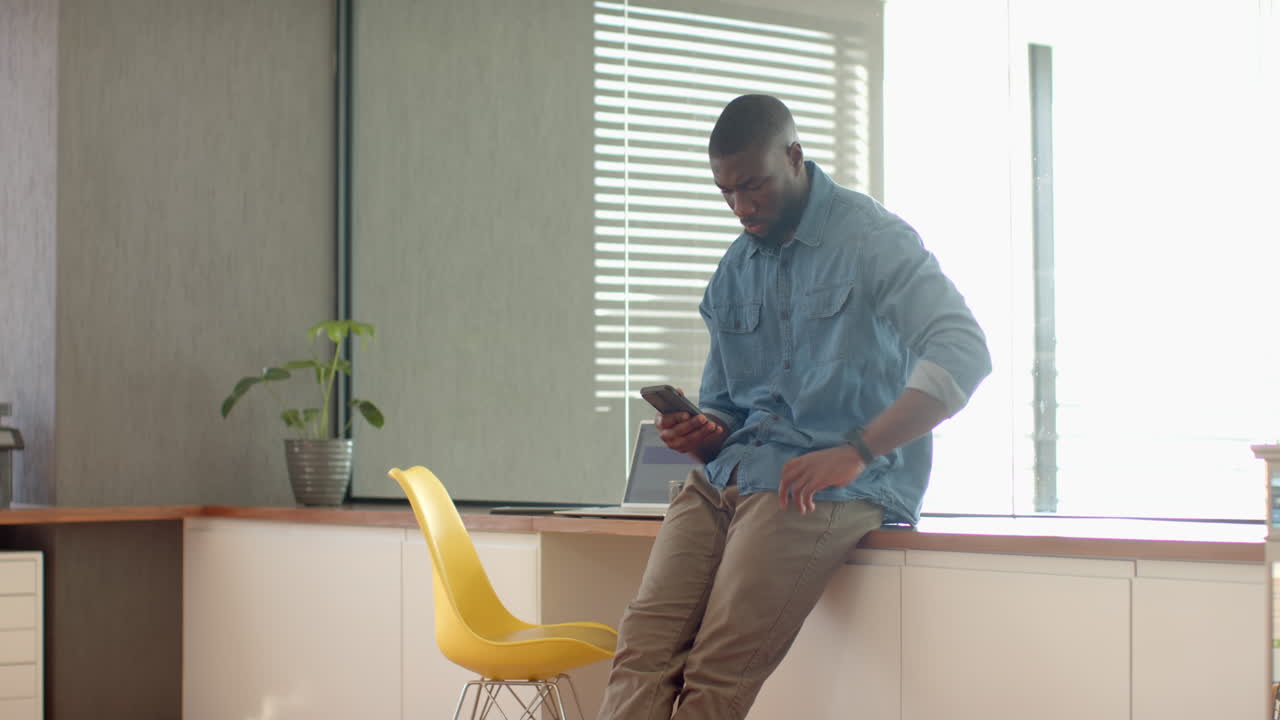 Using smartphone, man sitting on kitchen counter next to yellow chair