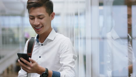 Junger-Asiatischer-Geschäftsmann,-Der-Bei-Der-Arbeit-Im-Büro-Sein-Smartphone-Nutzt-Und-SMS-Nachrichten-Auf-Dem-Mobiltelefon-Sendet