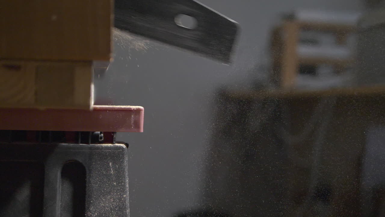Slow motion footage ( 120 fps ) of  saw cutting through large plank of wood as sawdust floats through the air, slowly drifting down