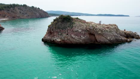 Vista-Aérea-Giratoria-Cerca-De-La-Playa-De-Metalia-Con-Agua-Turquesa-Y-Una-Pequeña-Isla-Rocosa,-Thassos,-Grecia,-Europa