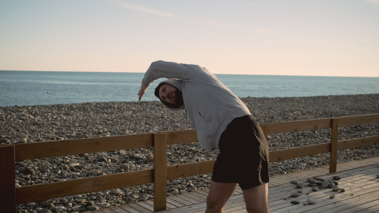 hombre estirándose en un paseo marítimo de la playa