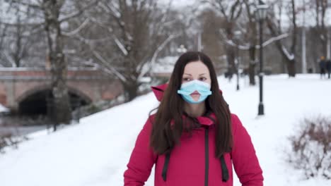mujer de pie en el parque de la ciudad nevada con una máscara facial con agujero durante el invierno