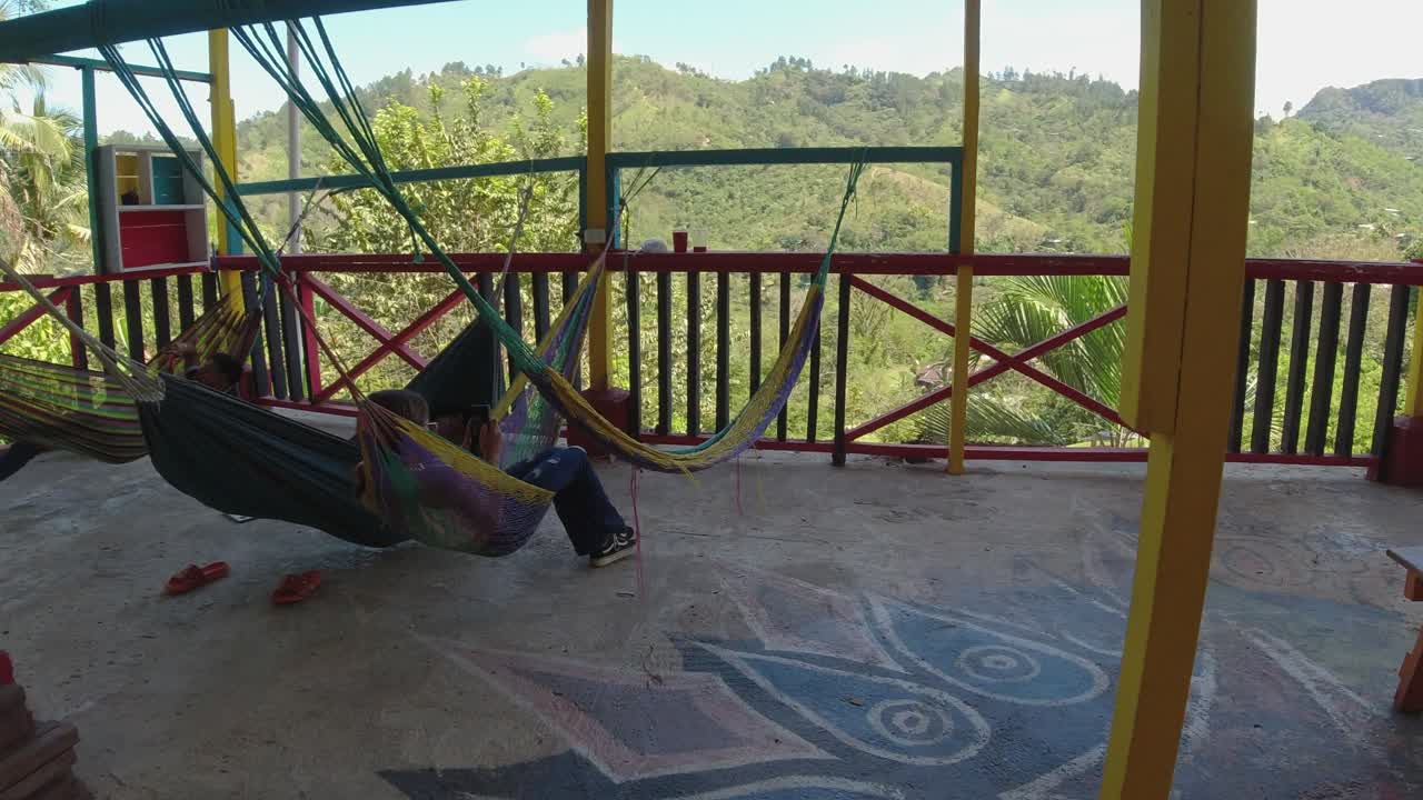 una mujer joven relajada en una hamaca en la terraza del balcón revisa su teléfono