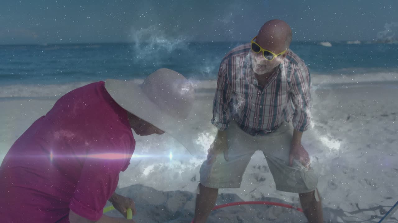 Senior couple beach, woman picking up ring while man leaning, nebula flares passing for travel play