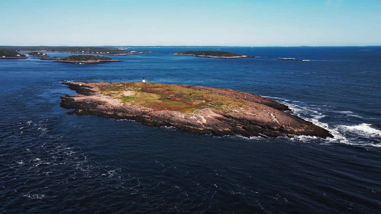 メイン州ポプハムビーチ近くの小さな島にある歴史的なポンド島灯台を映し出すスムーズなドローンショット。ケネベック川の河口にある岩だらけの島にはカモメが飛び交い、波が打ち寄せている。