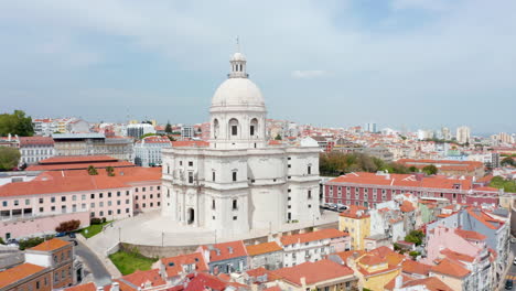 Close-up-aerial-view-of-beautiful-white-church-on-the-hill-surrounded-by-colorful-houses-in-urban-city-center-of-Lisbon,-Portugal