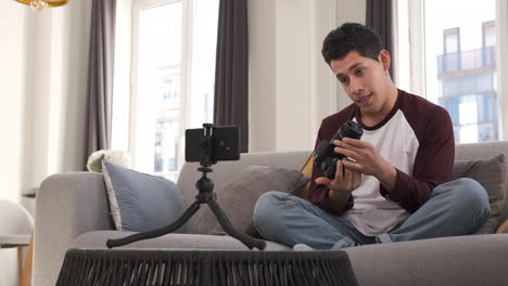 young latin man talking on mobile camera, explaining a photo camera. content creator concept
