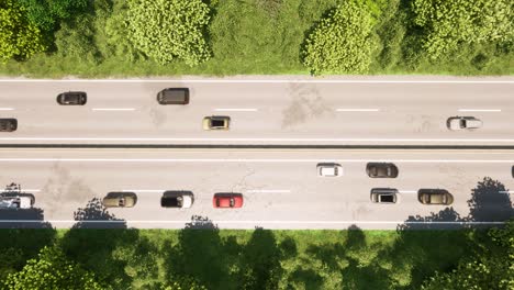 Highway-with-two-lanes-in-both-directions,-inside-a-forest,-with-cars-passing-by-3D-animation-top-view-dolly-right-slowly