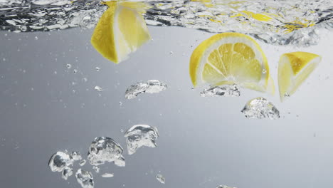 Underwater-shot-of-lemon-quarters-falling-in-fresh-clear-water-with-big-bubbles