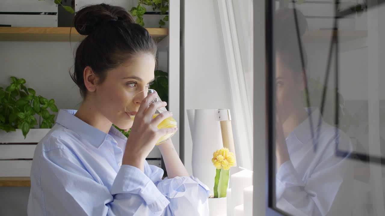 집 에서 오렌지 주스 를 마시고 창문 을 통해 보고 있는 젊은 여자