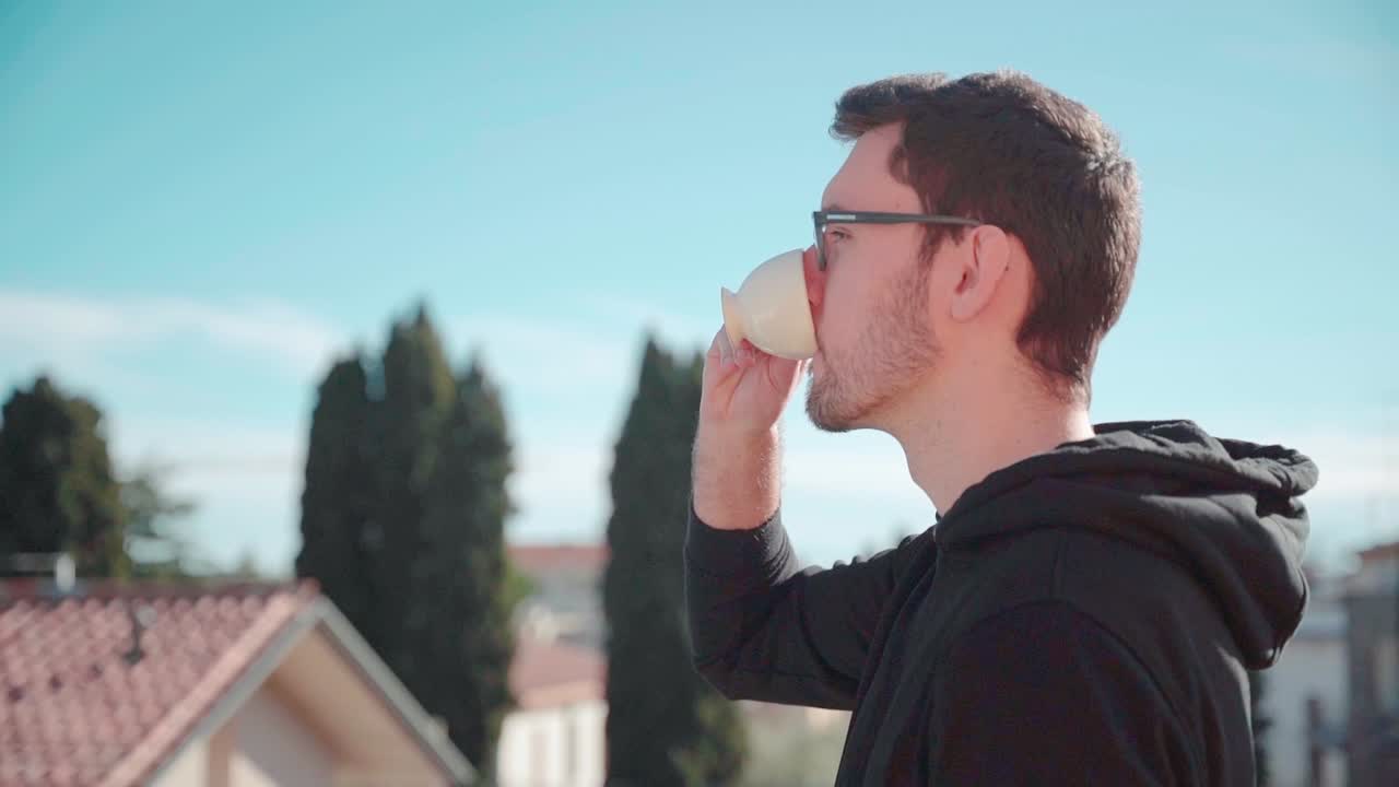 Young man drinking coffee espresso in sun on balcony