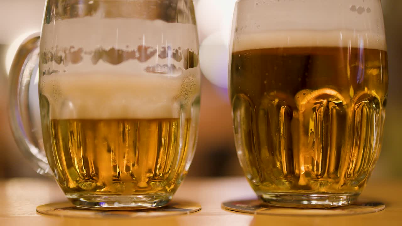 A hand lifts a foamy lager mug from a wooden table in a Czech brewpub