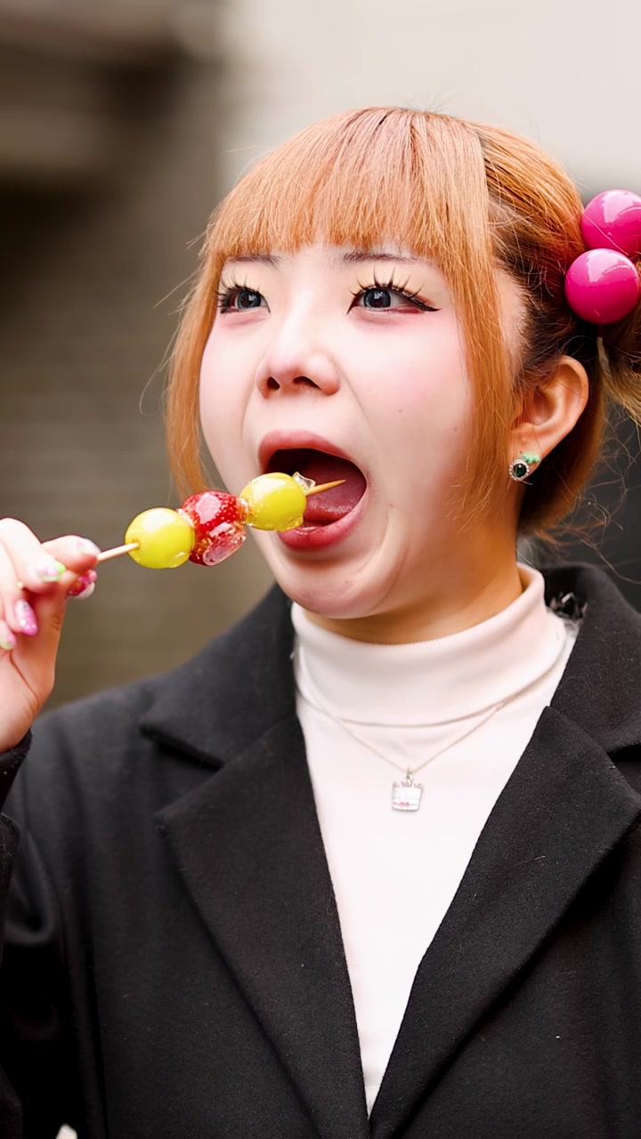야외에서 탕후루 딸기 포도 꼬치를 즐기는 세련된 아시아 여성의 클로즈업