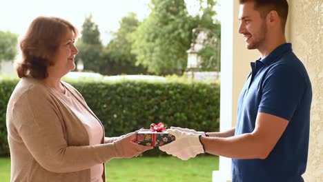 a heartwarming moment of gift-giving: a smiling young man presents a beautifully wrapped present to a delighted woman at her doorstep in a bright, peaceful setting