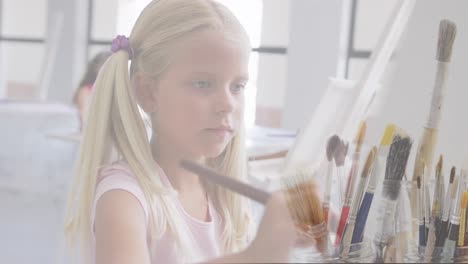 animation of paint brushes over caucasian schoolgirl painting in art class