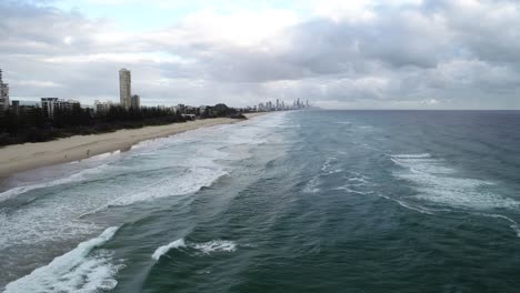 Langsame-Luftaufnahmen-Eines-Strandes-Bei-Sonnenaufgang-Mit-Weißem-Sand,-Wellenrollen,-Schwimmern-Und-Surfern-Und-Einem-Schönen-Strand-Mit-Zahlreichen-Türmen-Und-Gebäuden