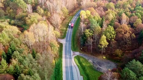 Aerial-Shot-of-a-Two-Trucks-Driving-On-a-Road-In-Colorful-Autumn-Forest