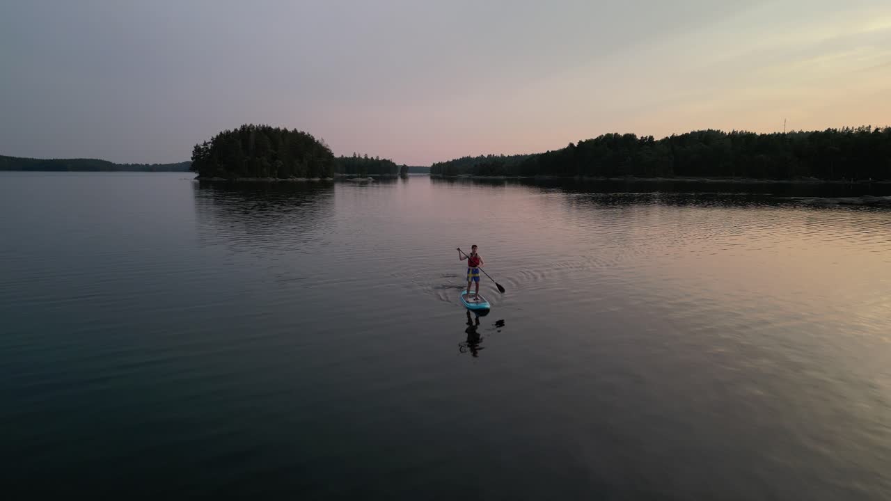 Flyover man paddleboarding on calm lake, Sweden