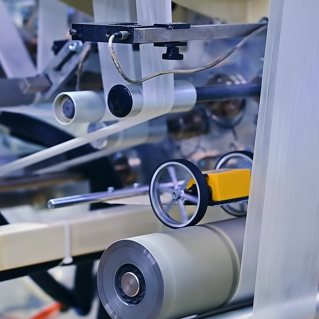 Numerous shafts - big and small rotating quickly to pass the inner layer of diapers. The white fabric goes through many rollers at the enterprise. Close up