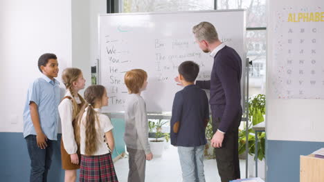 multiethnic students group standing in front of the blackboard while the teacher teaches them the pronouns in the english classroom