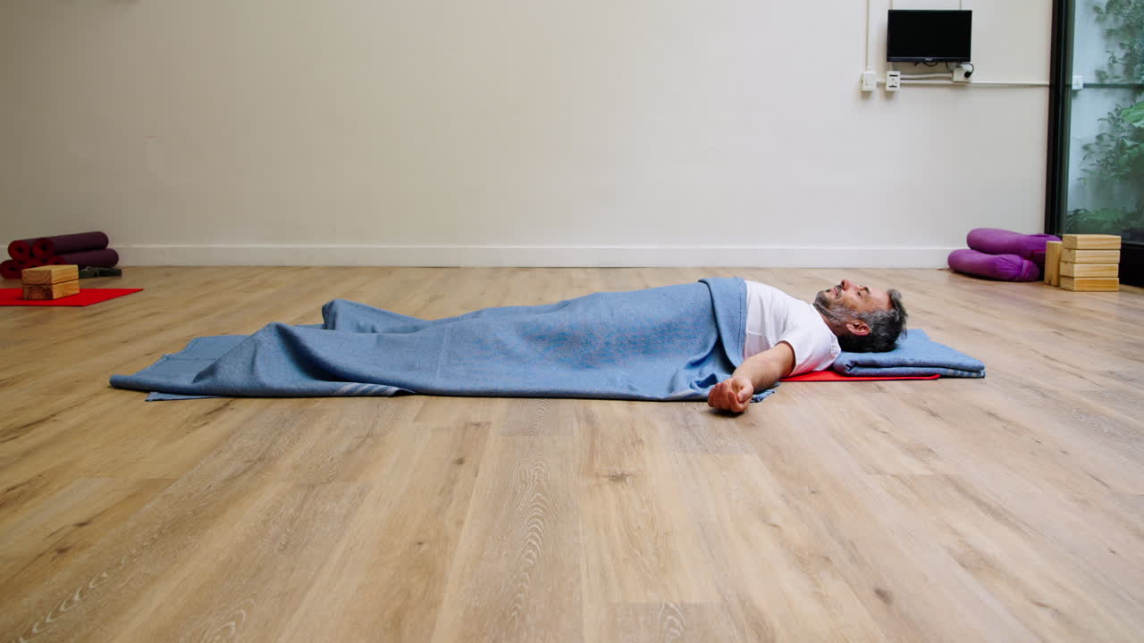 Mies lepää Savasana-asennossa joogamatolla studiossa