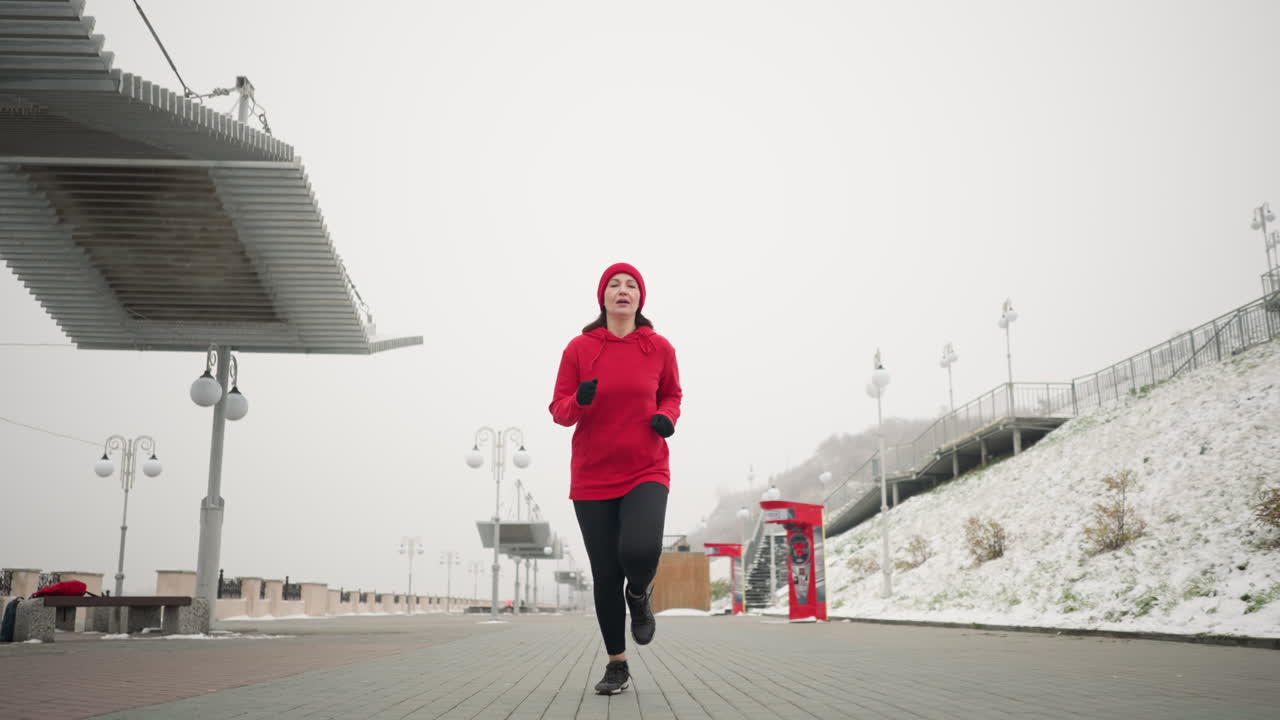 Coach jogging outdoors on interlocked pavement during winter, serene environment with benches, a snowy hill nearby, and modern urban features like lamp posts and a bag on one of the benches