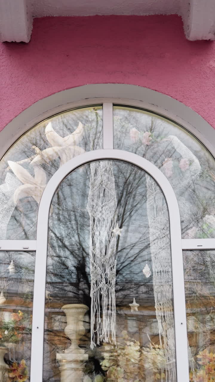 vista de cerca de una casa de color rosa, con ventanas decorativas con diseños intrincados, con un recipiente de flores visto a través del vidrio de la ventana