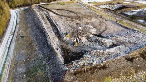 Aerial-flyover-landfill-full-of-trash,-pollution-environmental-problem,-garbage,-trucks-dump-waste-products-polluting-in-a-dump,-wide-angle-revealing-drone-shot-moving-backward