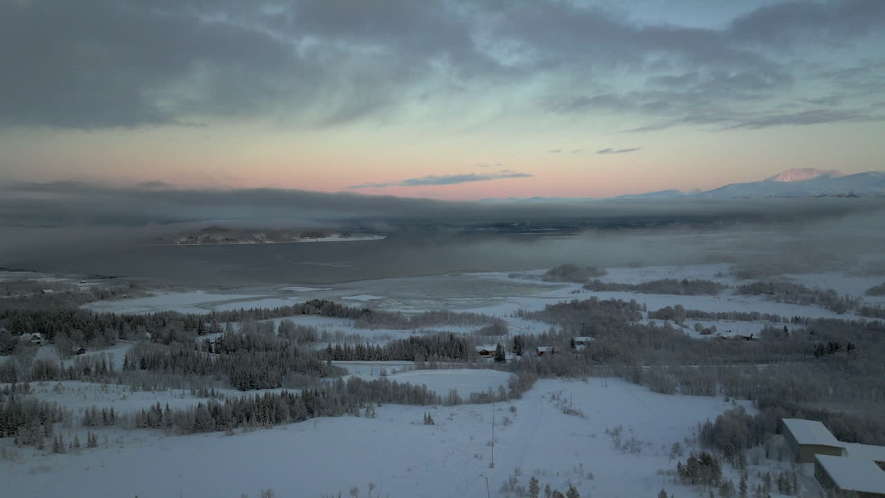 Colorful sky at sunset as drone flies over snowy Kvaloya landscape, Norway