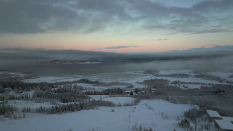 Colorful-sky-at-sunset-as-drone-flies-over-snowy-Kvaloya-landscape,-Norway