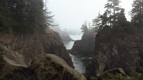 Aerial-view-backwards-through-a-misty-corridor-in-middle-of-steep-cliffs-of-Samuel-H