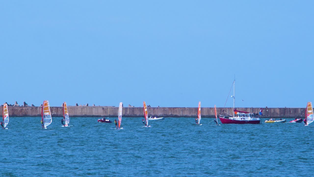 젊은 윈드서퍼 그룹이 지역 경쟁, 화려한 돛, 레크리에이션 수상 스포츠, 화창한 여름날, 라트비아의 고요한 발트해 카로스타 해변 만, 중간 거리 샷