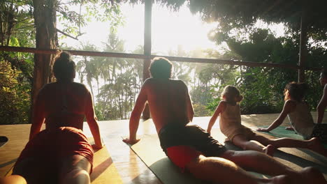 close up shot of a family of travelers enjoying a sunset meditation and yoga session on a wooden porch overlooking the rainforest and jungle leading out to the beach.